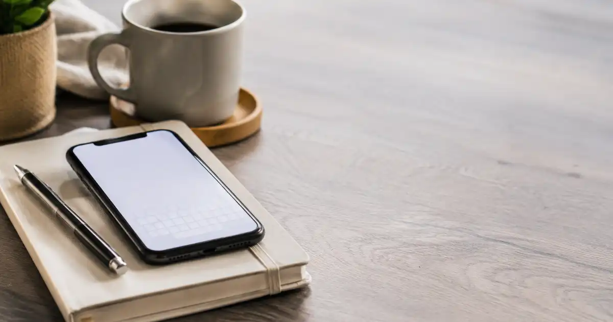 **Alt text:** Smartphone on a notebook beside a coffee cup on a calm, neutral-toned desk, representing a thoughtful farewell or encouragement message.